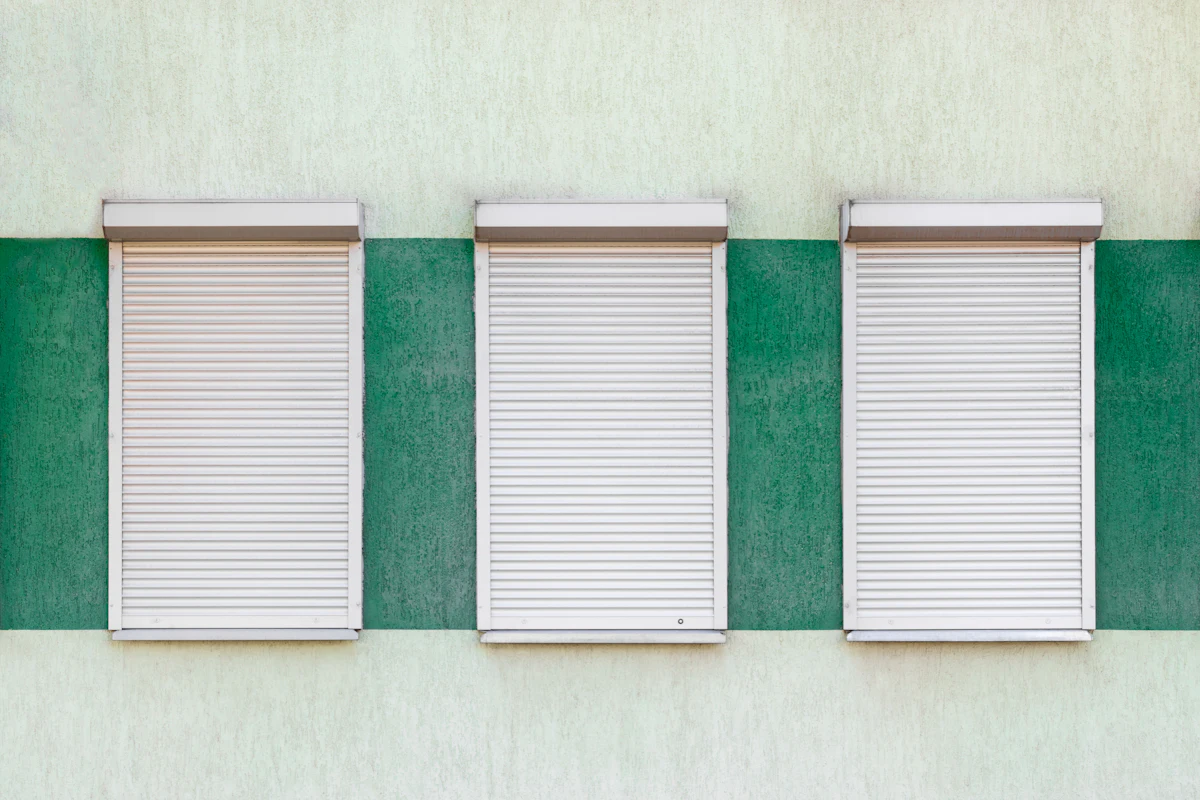 Três janelas com estores brancos numa fachada verde